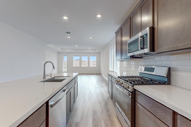 kitchen with sink, light wood-type flooring, tasteful backsplash, dark brown cabinets, and stainless steel appliances