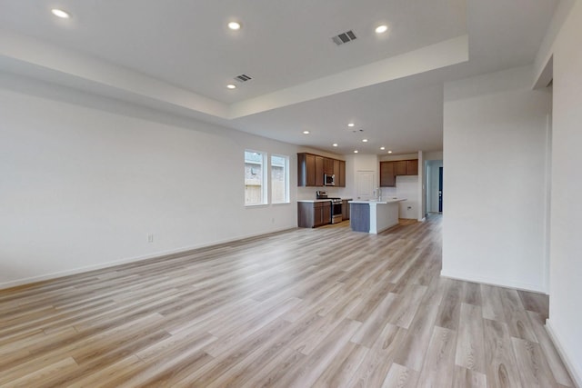 unfurnished living room with a raised ceiling and light hardwood / wood-style flooring