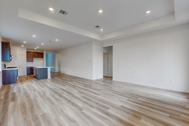 unfurnished living room featuring a raised ceiling, light hardwood / wood-style flooring, and sink