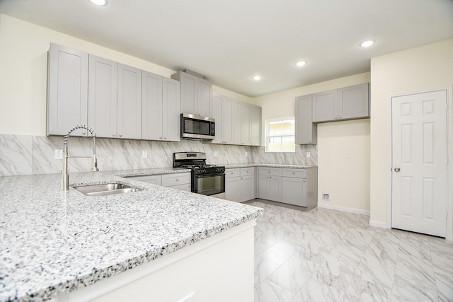 kitchen featuring decorative backsplash, light stone counters, gray cabinetry, stainless steel appliances, and sink