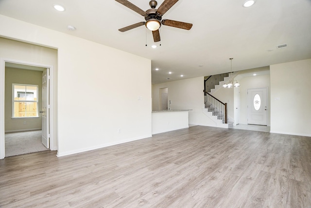 unfurnished living room with ceiling fan with notable chandelier and light hardwood / wood-style floors