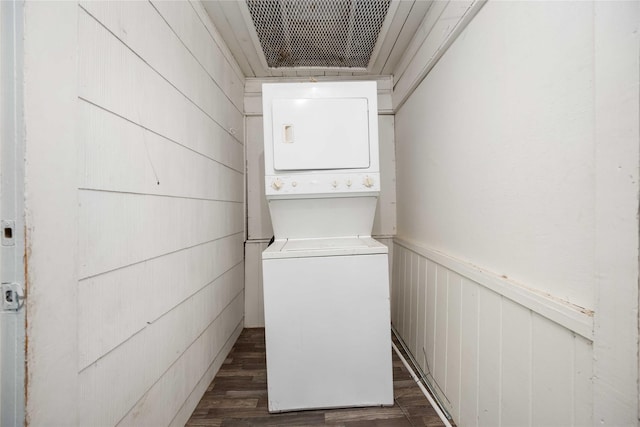 laundry room featuring wooden walls, stacked washer / dryer, and dark wood-type flooring