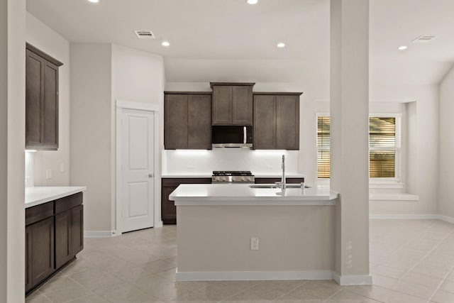 kitchen featuring a center island with sink, sink, light tile patterned floors, dark brown cabinetry, and stainless steel appliances