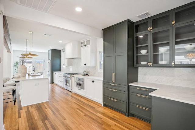 kitchen featuring tasteful backsplash, premium range hood, sink, pendant lighting, and white cabinets