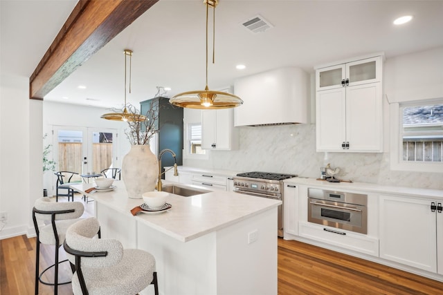 kitchen with appliances with stainless steel finishes, custom exhaust hood, sink, pendant lighting, and a center island with sink