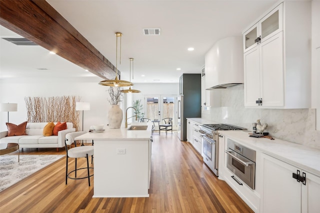 kitchen featuring hardwood / wood-style floors, custom exhaust hood, white cabinets, appliances with stainless steel finishes, and decorative light fixtures