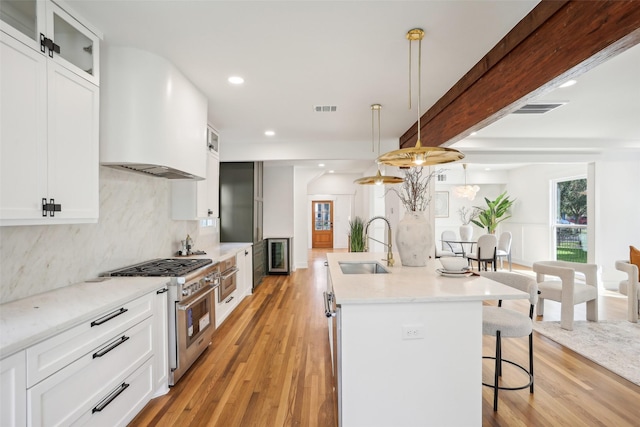 kitchen with stainless steel appliances, light hardwood / wood-style flooring, hanging light fixtures, and a center island with sink