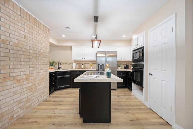 kitchen featuring tasteful backsplash, brick wall, a kitchen island, black appliances, and light wood-type flooring