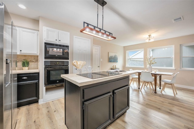 kitchen with a center island, backsplash, black appliances, white cabinets, and hanging light fixtures