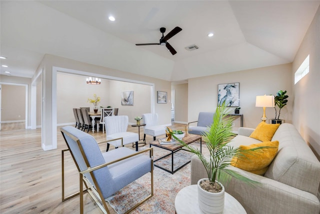 living room featuring a raised ceiling, ceiling fan with notable chandelier, light hardwood / wood-style flooring, and vaulted ceiling