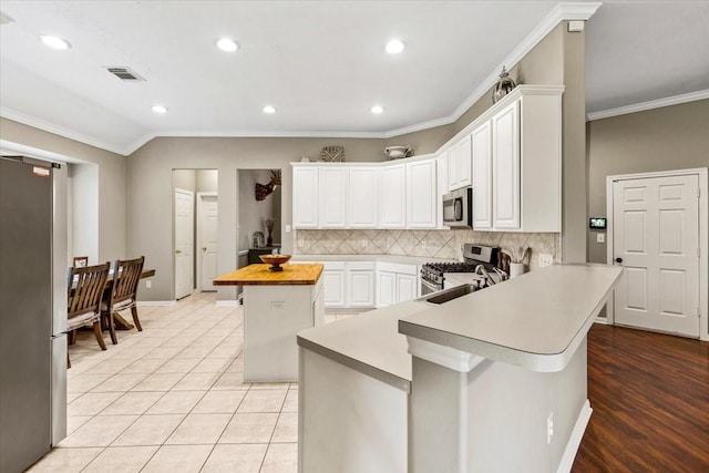 kitchen with a center island, appliances with stainless steel finishes, crown molding, white cabinets, and light wood-type flooring