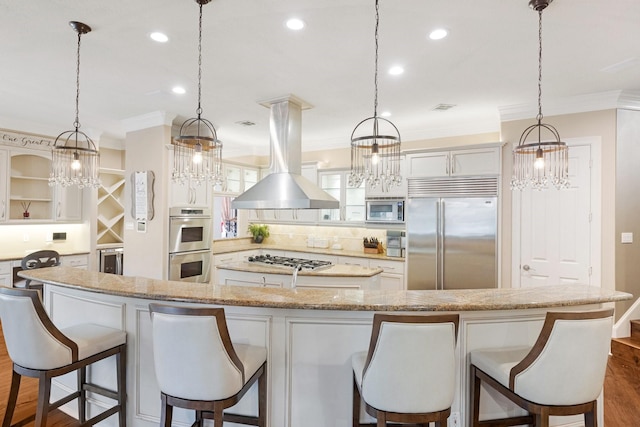 kitchen featuring built in appliances, decorative light fixtures, island range hood, and a kitchen bar