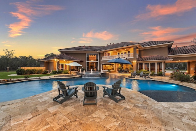 pool at dusk featuring an in ground hot tub, pool water feature, and a patio area