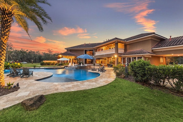 pool at dusk with an in ground hot tub, a patio, and a lawn