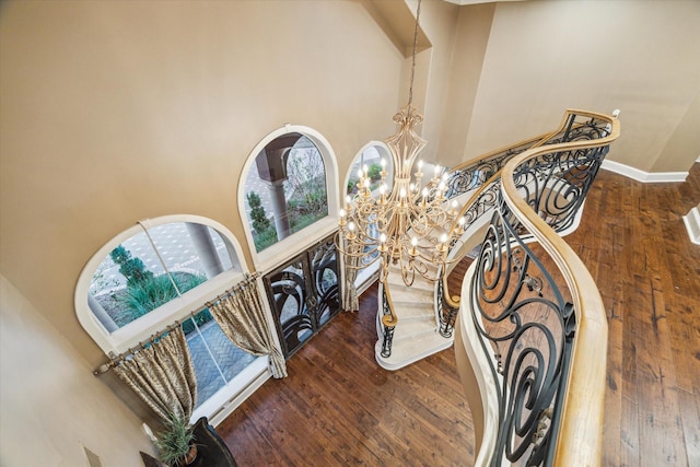 stairs with a towering ceiling, hardwood / wood-style flooring, and a notable chandelier