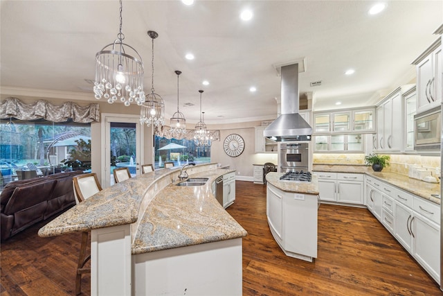 kitchen with sink, ventilation hood, a large island with sink, pendant lighting, and a breakfast bar