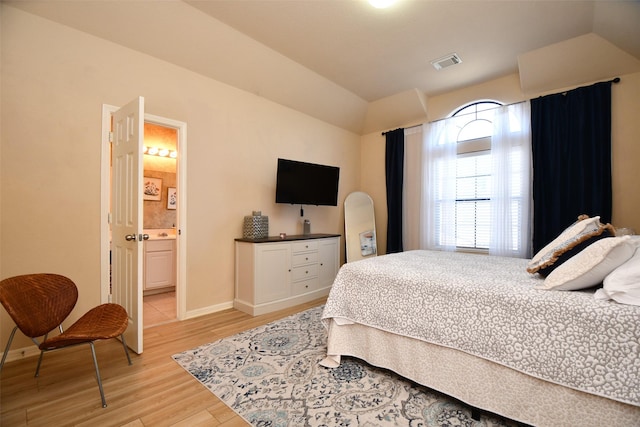 bedroom featuring light hardwood / wood-style flooring, ensuite bath, and lofted ceiling