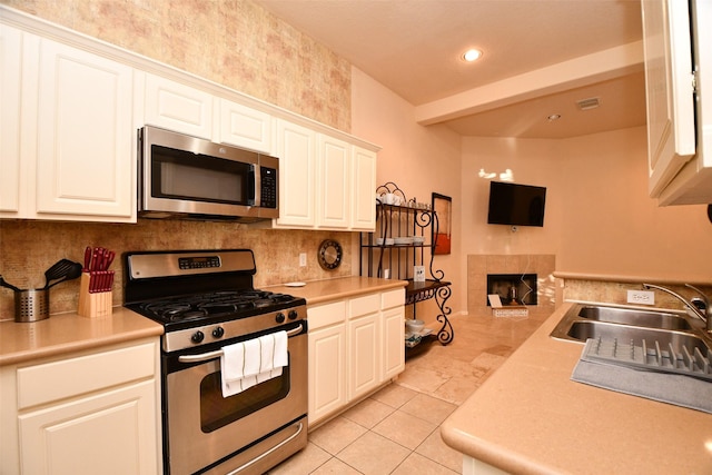 kitchen with white cabinetry, sink, a tiled fireplace, light tile patterned floors, and appliances with stainless steel finishes