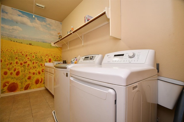 laundry room featuring washing machine and dryer, light tile patterned floors, and cabinets