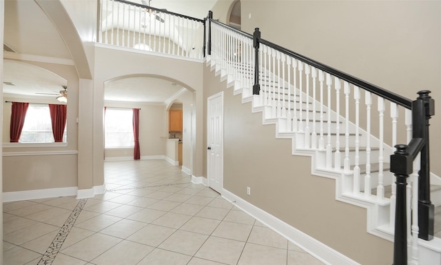 stairs with tile patterned floors, ceiling fan, ornamental molding, and a high ceiling