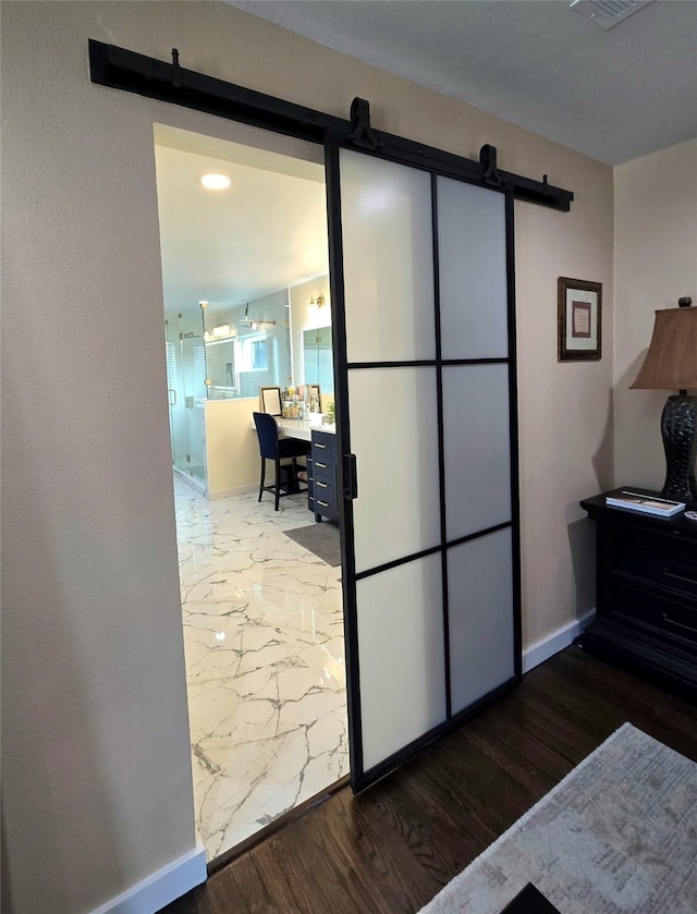 bedroom with a barn door, visible vents, baseboards, and wood finished floors