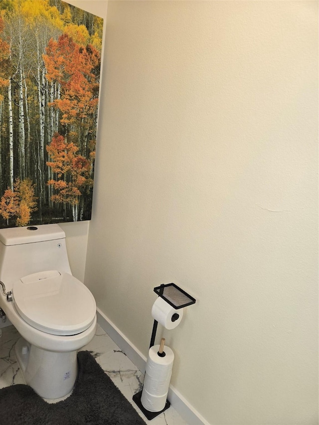 bathroom with toilet, marble finish floor, and baseboards