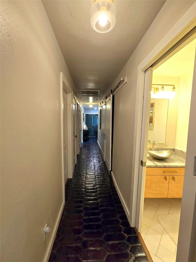 corridor with visible vents, a sink, baseboards, and a barn door