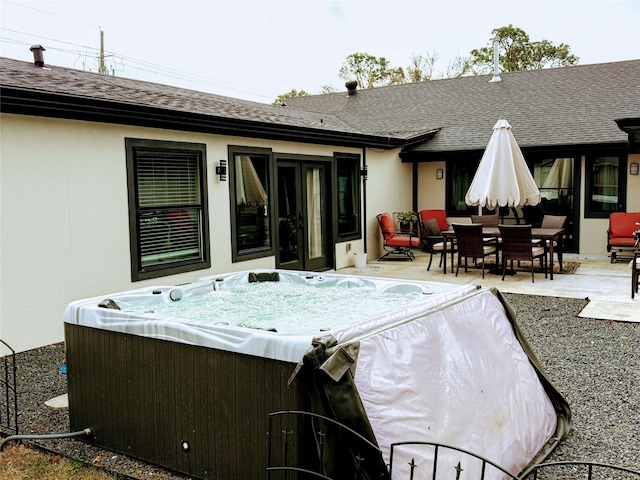 back of property featuring a hot tub, a shingled roof, outdoor dining area, a patio area, and stucco siding