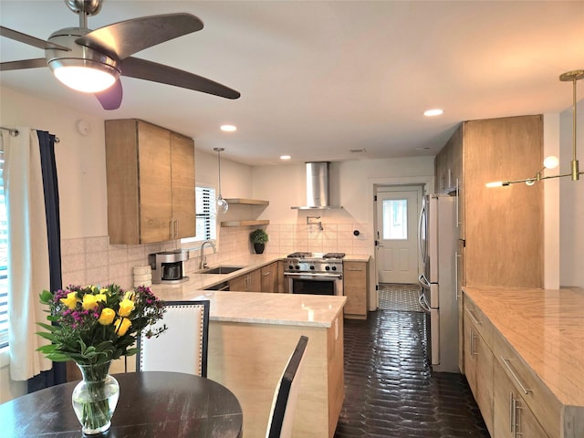 kitchen featuring wall chimney range hood, decorative light fixtures, stainless steel appliances, and kitchen peninsula