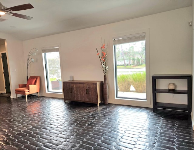 living area with baseboards, stone finish flooring, a wealth of natural light, and a ceiling fan