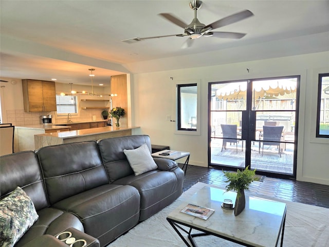 living area with a wealth of natural light, a ceiling fan, visible vents, and baseboards