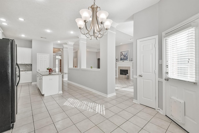 kitchen with white cabinetry, an inviting chandelier, black fridge, decorative light fixtures, and a kitchen island