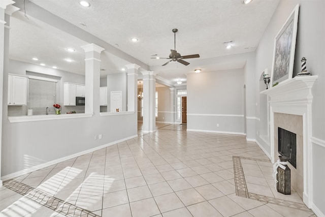 unfurnished living room with ornate columns, a textured ceiling, ceiling fan, a tiled fireplace, and light tile patterned flooring