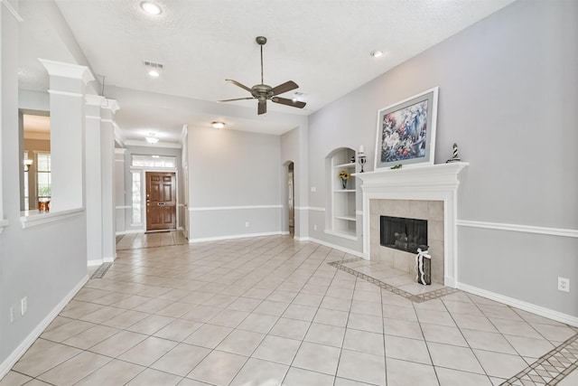 unfurnished living room with a textured ceiling, ceiling fan, light tile patterned floors, built in features, and a tiled fireplace