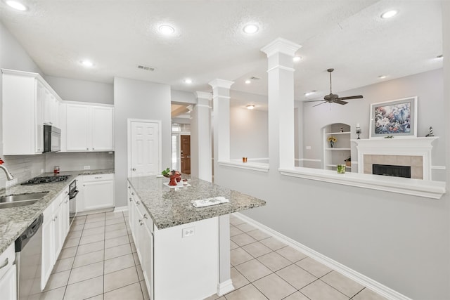 kitchen with ceiling fan, a center island, stainless steel dishwasher, a tiled fireplace, and white cabinets