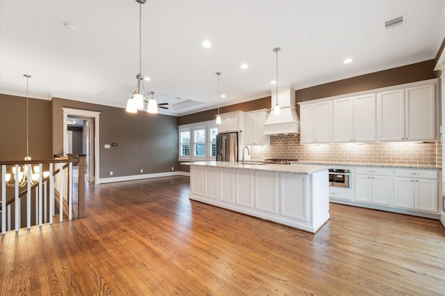 kitchen with premium range hood, white cabinets, a center island with sink, light hardwood / wood-style floors, and stainless steel appliances