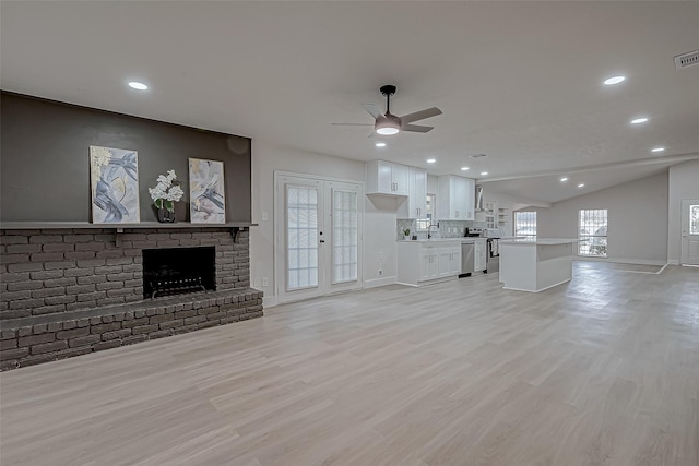 unfurnished living room with vaulted ceiling, ceiling fan, french doors, a brick fireplace, and sink