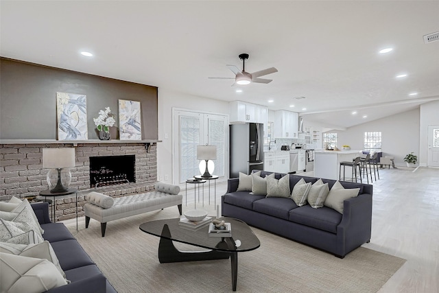 living room with lofted ceiling, a fireplace, ceiling fan, and light hardwood / wood-style flooring