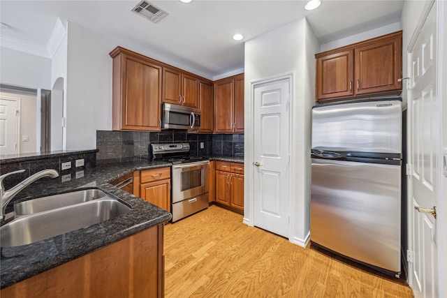 kitchen with appliances with stainless steel finishes, tasteful backsplash, dark stone counters, sink, and light hardwood / wood-style flooring