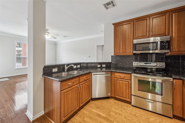 kitchen featuring sink, stainless steel appliances, light hardwood / wood-style flooring, dark stone countertops, and crown molding