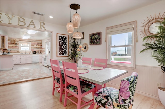 dining area with wood walls, light hardwood / wood-style floors, and sink