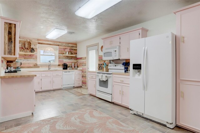 kitchen with a textured ceiling, white appliances, sink, white cabinetry, and wood walls