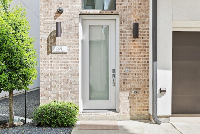 doorway to property featuring a garage and brick siding