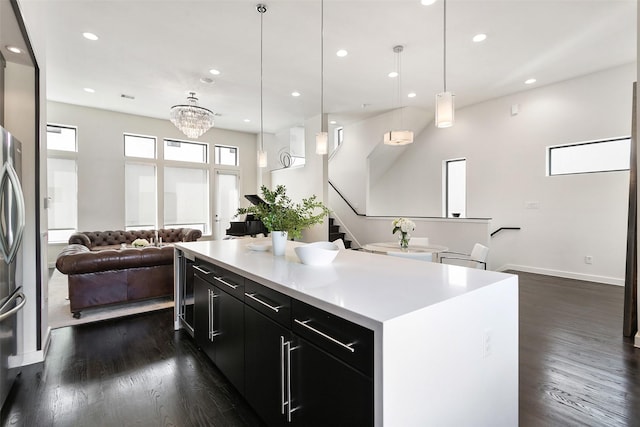 kitchen featuring a kitchen island, open floor plan, light countertops, hanging light fixtures, and dark cabinetry