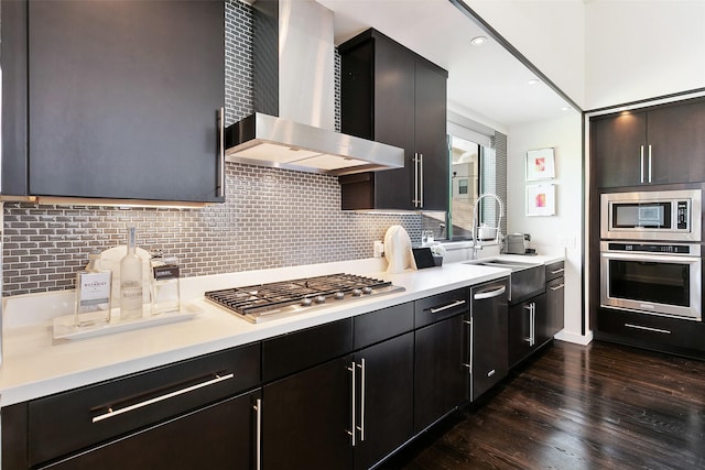 kitchen with sink, wall chimney exhaust hood, dark hardwood / wood-style floors, decorative backsplash, and appliances with stainless steel finishes