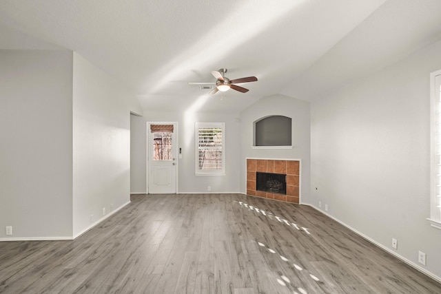 unfurnished living room featuring wood-type flooring, vaulted ceiling, ceiling fan, and a tiled fireplace