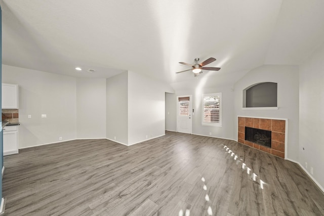 unfurnished living room featuring ceiling fan, light wood-type flooring, a tile fireplace, and vaulted ceiling