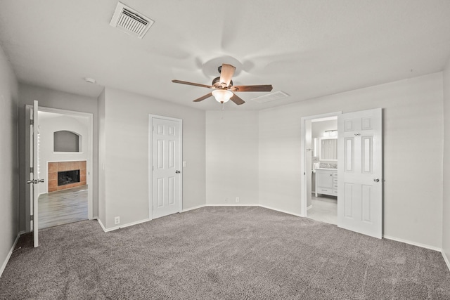 unfurnished bedroom featuring ensuite bathroom, ceiling fan, carpet floors, and a fireplace