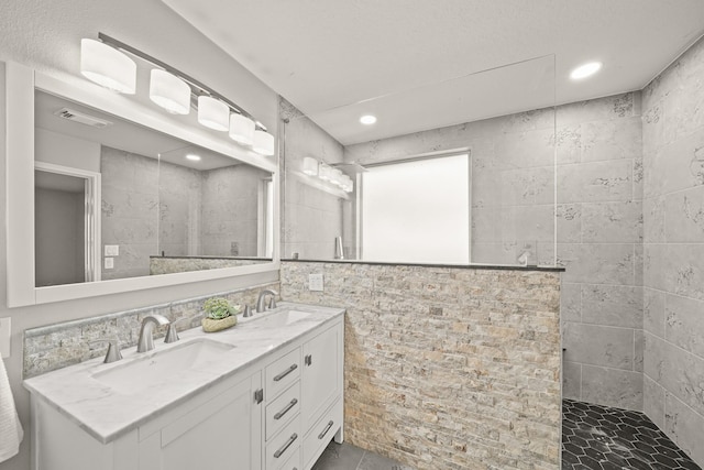 bathroom featuring a tile shower, vanity, and tile walls