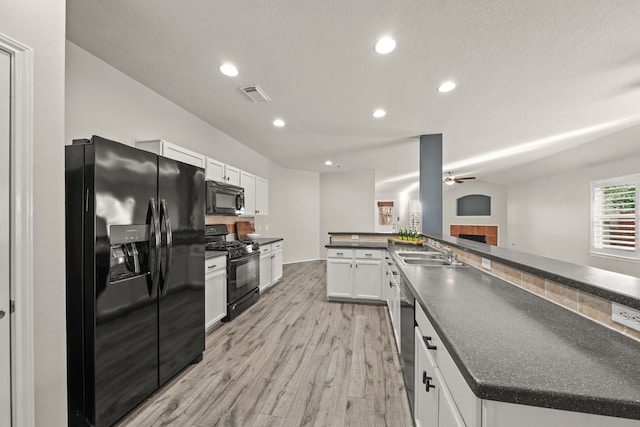 kitchen with kitchen peninsula, sink, black appliances, white cabinetry, and a tiled fireplace